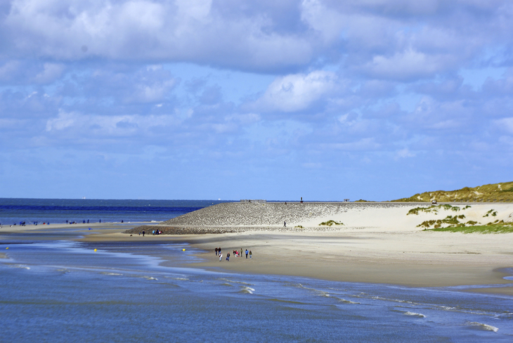 Strandlandschaft mit Dünen und Meer unter blauem Himmel.
