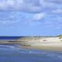 Strandlandschaft mit Dünen und Meer unter blauem Himmel.