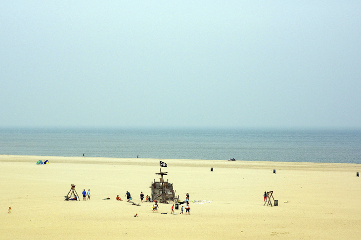 Strand mit Sandfläche und Spielgeräten, dahinter das Meer bei diesigem Himmel.