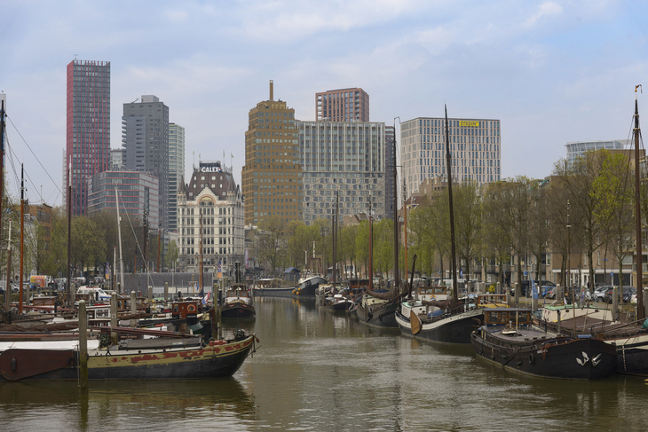 Hafenkanal mit historischen Schiffen und moderner Skyline in Rotterdam.