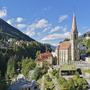 Kirche in Bad Gastein, umgeben von Bergen und Häusern unter blauem Himmel.