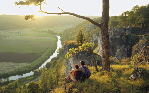 Zwei Wanderer genießen den Ausblick über das Altmühltal bei Sonnenuntergang.
