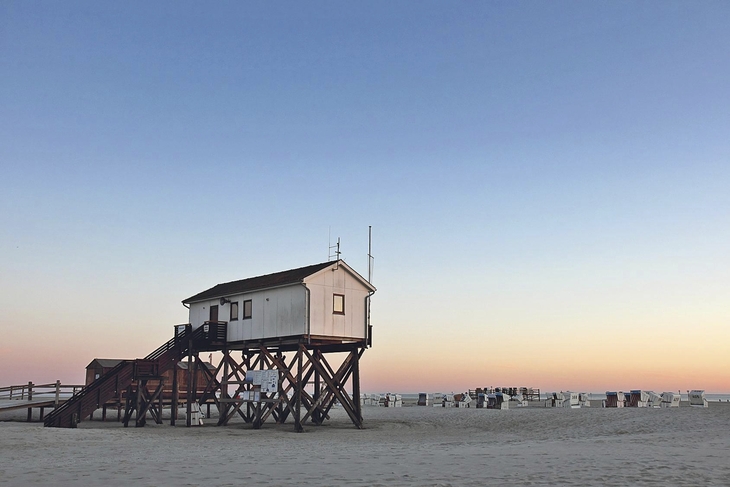 Pfahlbau und Strandkörbe am Strand von St. Peter-Ording bei Sonnenuntergang.