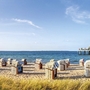 Strandkörbe am Timmendorfer Strand mit Seebrücke im Hintergrund und Seegras im Vordergrund, bei leichtbewölktem Himmel.