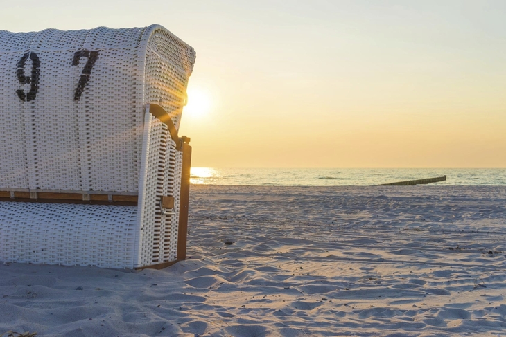 Strandkorb bei Sonnenuntergang am Strand mit Meereshorizont im Hintergrund.