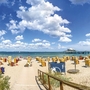 Blick vom Weg zwischen den mit Seegras bewachsenen Dünen auf den Strand mit Strandkörben, dem Meer und blauem Himmel mit Wolken am Timmendorfer Strand.
