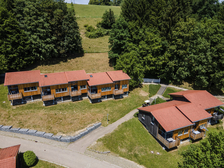Ferienhäuser mit roten Dächern in einer grünen, bewaldeten Landschaft.
