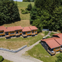 Ferienhäuser mit roten Dächern in einer grünen, bewaldeten Landschaft.