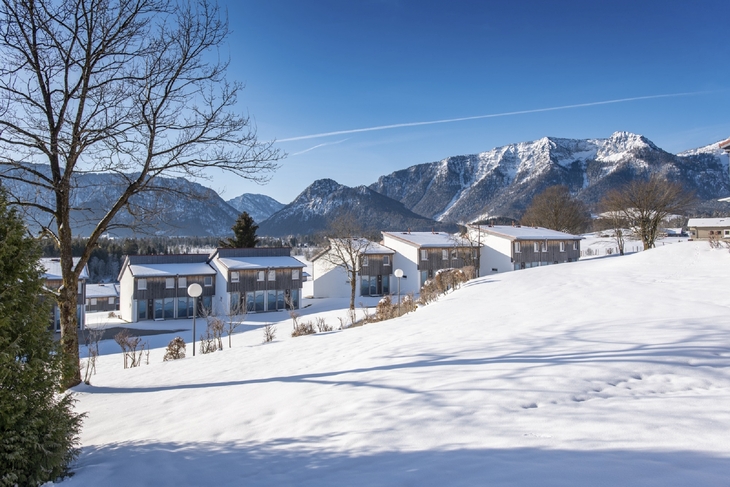 Schneebedeckte Landschaft mit Häusern vor Bergkulisse im Winter.