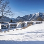 Schneebedeckte Landschaft mit Häusern vor Bergkulisse im Winter.