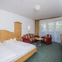 Hotelzimmer mit Doppelbett, Sofa, Tisch und Fernseher, hell eingerichtet.