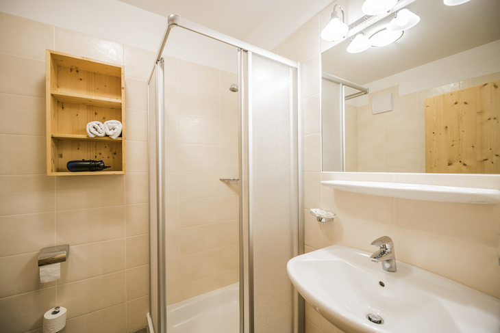 Helles Badezimmer mit Dusche, Waschbecken und Spiegel im Hotel Alpenrose.