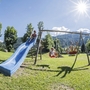 Kinder spielen auf einem Spielplatz mit Rutsche und Schaukel bei Sonnenschein.