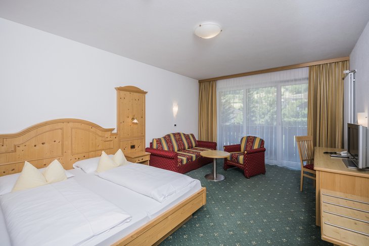 Hotelzimmer mit Doppelbett, Sofa, Tisch und Fernseher, hell eingerichtet.