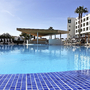 Hotelpool mit Sonnenschirmen und Palmen bei klarem Himmel.