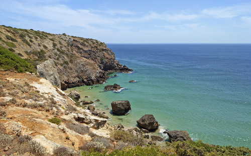Küste mit Klippen und blauem Meer unter klarem Himmel.