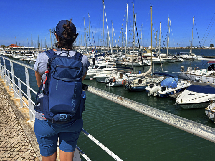 Person mit Rucksack blickt auf einen Hafen mit Segelbooten an der Algarve.