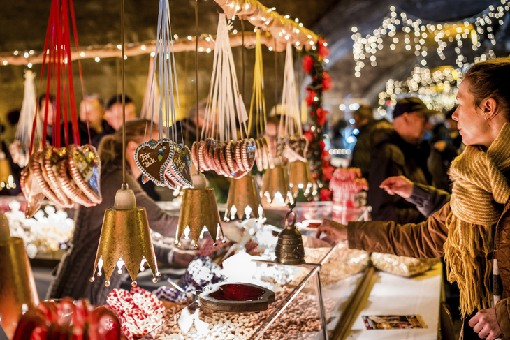 Marktstand mit weihnachtlicher Dekoration und Besuchern im Kerzenlicht.