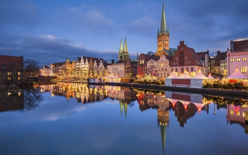 Abendlicher Blick auf einen beleuchteten Weihnachtsmarkt in Lübeck, mit Kirchturmhintergrund.
