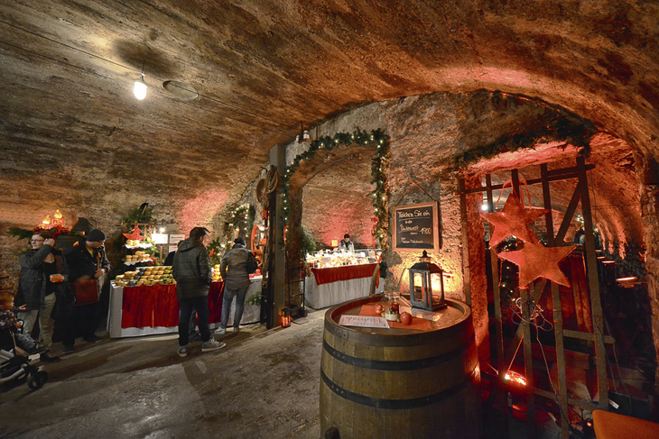 Weihnachtsmarkt in einem Weinkeller mit dekorierten Ständen und Besuchern.