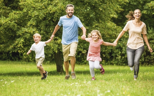 Familie läuft fröhlich im Park auf grüner Wiese.