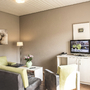 Wohnbereich in der Ferienanlage Büsum, mit Sofa, Sessel und kleinem Tisch, sowie einem Fernseher auf einem Sideboard.