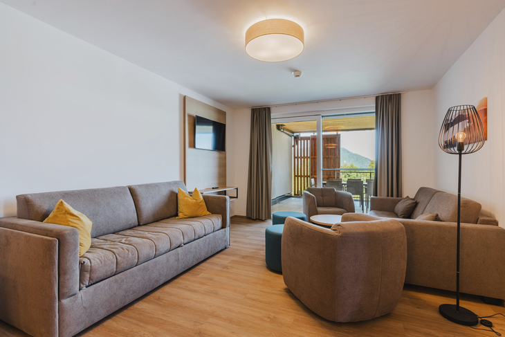 Modernes Wohnzimmer mit Sofa, Sesseln und Blick auf einen Balkon.