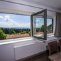 Blick aus einem geöffneten Fenster auf eine Waldlandschaft und blauen Himmel.