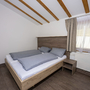 Kleines Schlafzimmer mit Doppelbett, Holzbalkendecke und Fenster mit Vorhang.