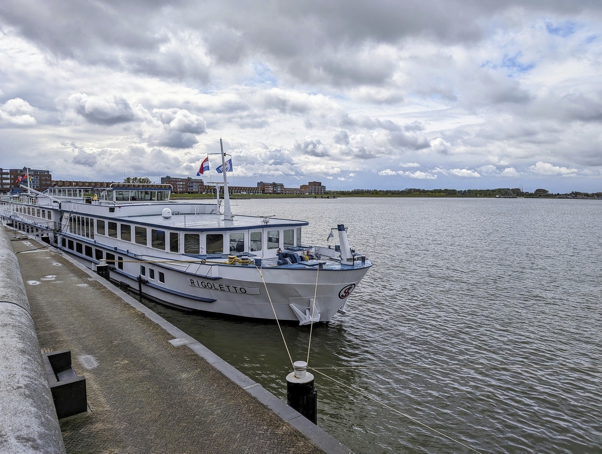 Flusskreuzfahrtschiff MS Rigoletto am Ufer unter bewölktem Himmel.