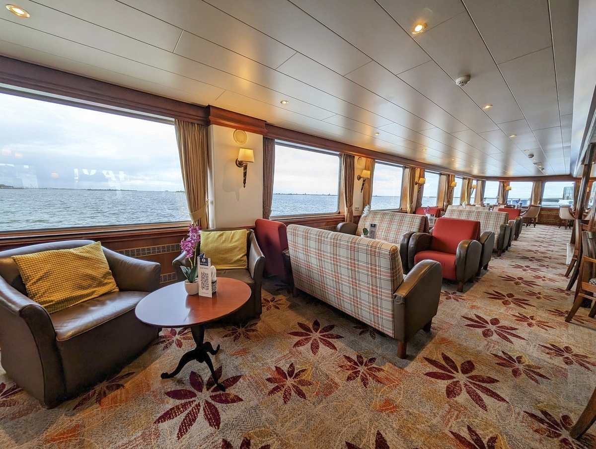 Sitzbereich auf einem Kreuzfahrtschiff mit großen Fenstern und Meerblick.