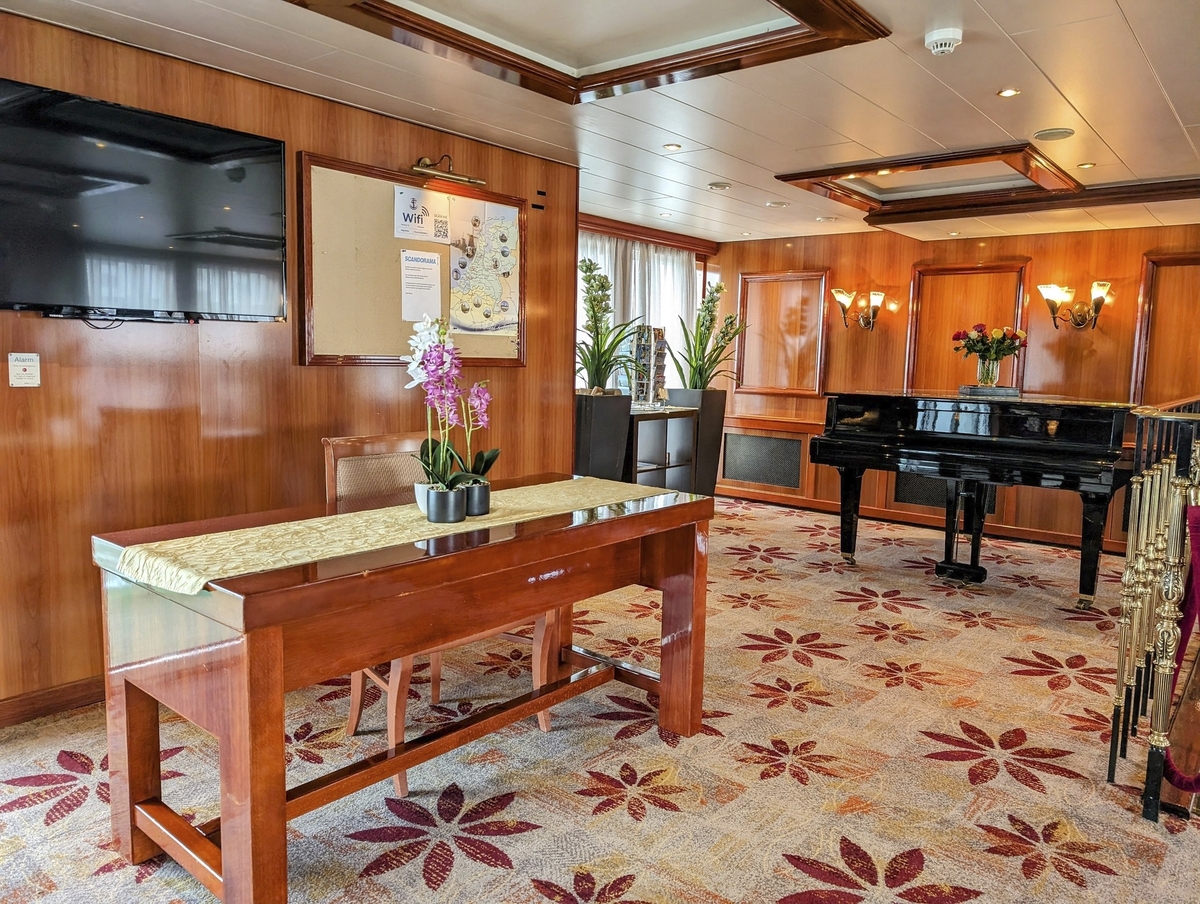 Salon auf einem Schiff mit Tisch, Fernseher und Klavier.