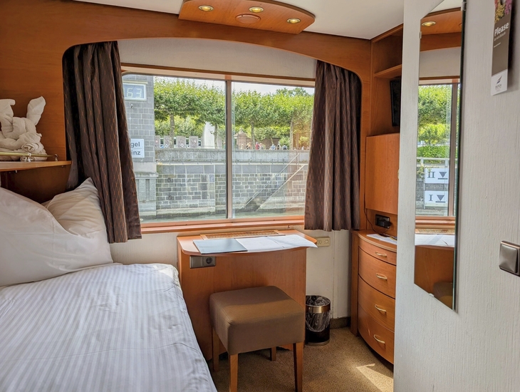 Einbettkabine auf einem Schiff mit Fenster, Spiegel und Schreibtisch.
