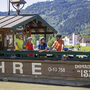 Radfahrer auf einer Fähre am Donau-Radweg, Berge im Hintergrund.