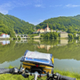 Blick auf eine Stadt am Fluss mit Brücke und bewaldeten Hügeln, Fahrradlenker im Vordergrund.