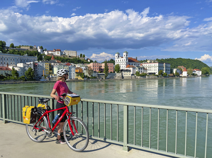 Radfahrerin auf einer Brücke mit Blick auf eine Stadt an der Donau bei klarem Himmel.