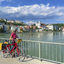 Radfahrerin auf einer Brücke mit Blick auf eine Stadt an der Donau bei klarem Himmel.