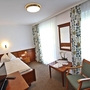 Einzelzimmer mit Bett, Tisch, Stuhl und Fenster mit Vorhängen im Landhotel Post Ebensee.