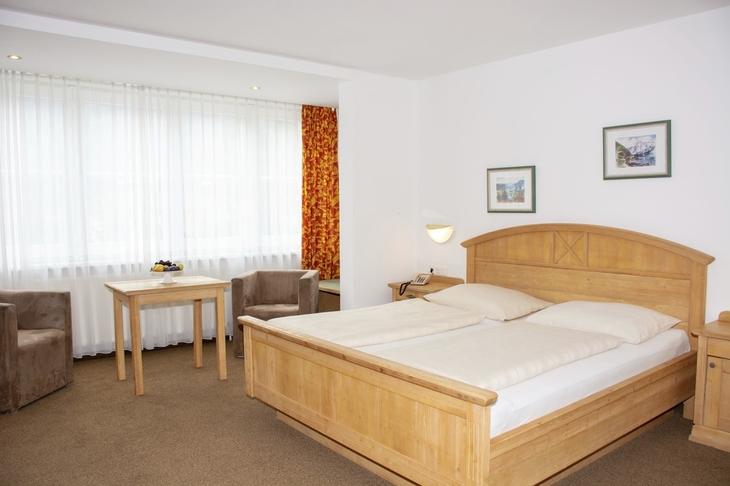 Helles Doppelzimmer mit Holzmöbeln und großem Fenster.