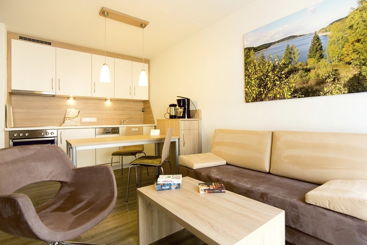 Wohnbereich mit Küche, Esstisch, Stühlen, Sofa, Sessel, Tisch und Wandbild in Ferienanlage Braunlage.