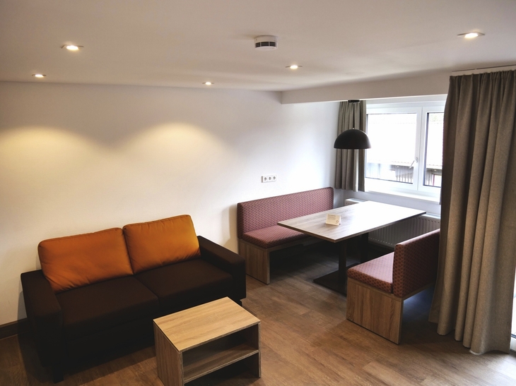 Wohnzimmer mit Sofa, Tisch, Eckbank und Fenster, moderne Beleuchtung.