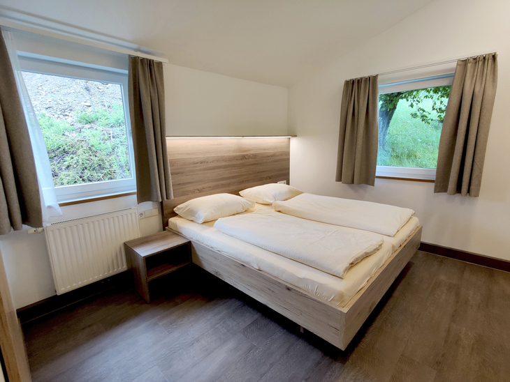 Renovierter Schlafraum mit Doppelbett und zwei Fenstern.