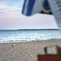 Rechts im Bild ein Teil von einem Strandkorb sowie ein Küstenstreifen der ins Meer ragt. Sandstrand mit Möven, dahinter das Meer bei leichter Dämmerung. 