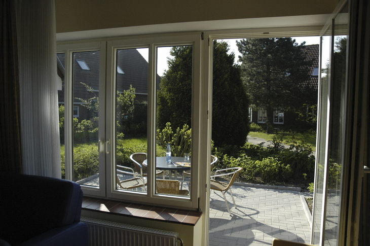Blick aus einem Wohnzimmer auf eine Terrasse mit Gartenmöbeln und grünem Garten.