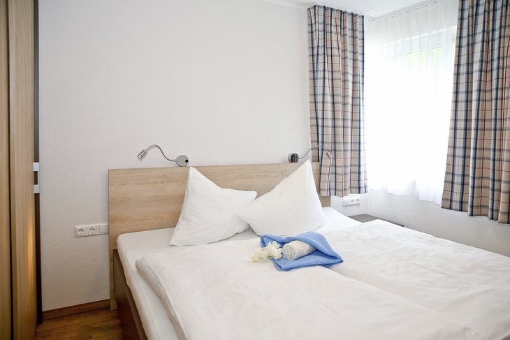 Helles Schlafzimmer mit Doppelbett und blauen Vorhängen.
