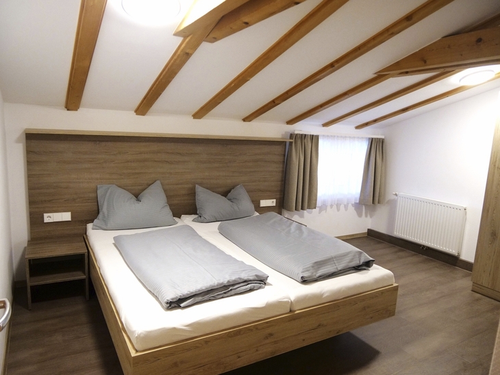 Schlafzimmer mit Doppelbett, Holzbalkendecke und Fenster mit Vorhängen.