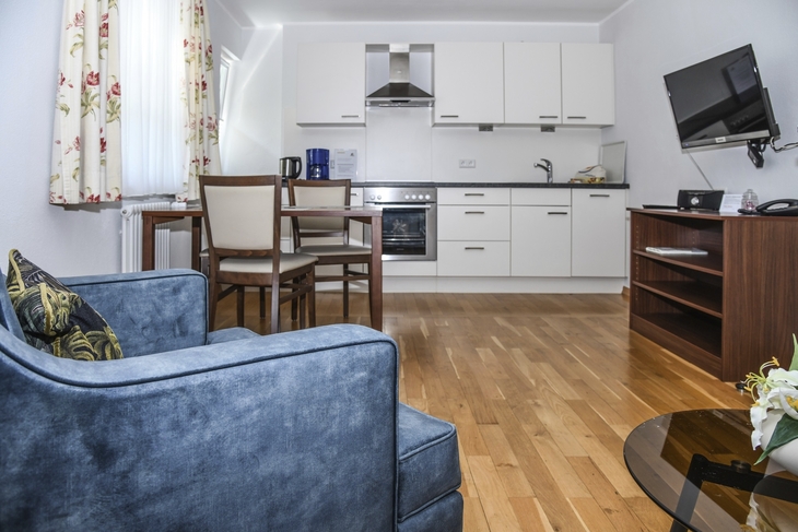 Wohnzimmer mit blauer Couch, Esstisch, Küche und Fernseher.