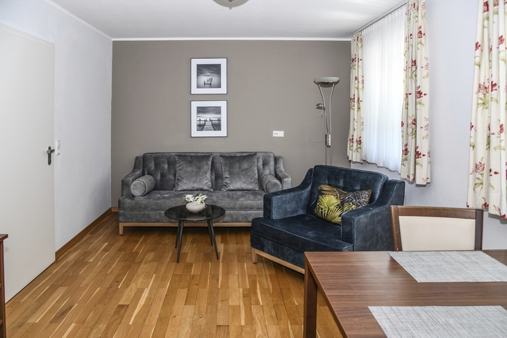 Wohnzimmer mit grauem Sofa, Sessel, Holztisch und dekorativen Wandbildern.