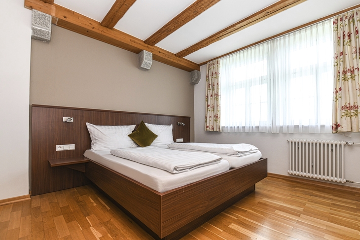 Schlafzimmer mit Holzbalkendecke, Doppelbett und großem Fenster.