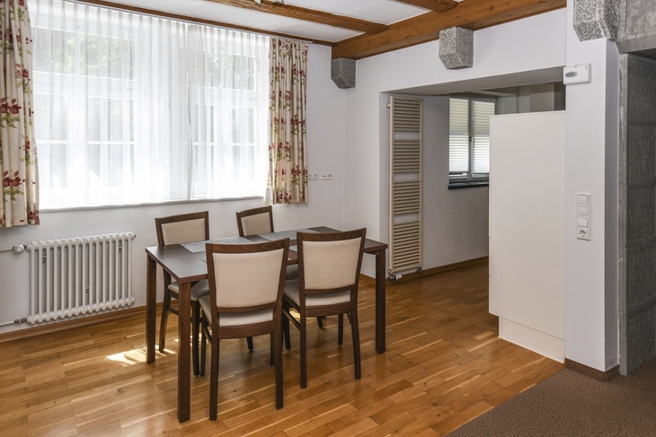 Essbereich mit Holztisch, vier Stühlen, Fenster mit Vorhängen und Holzboden.